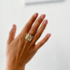 bague large avec des plis en or jaune portée sur une main avec un fond blanc