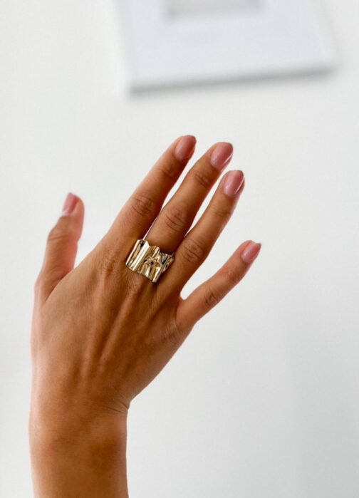 bague large avec des plis en or jaune portée sur une main avec un fond blanc