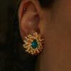 boucles d'oreilles en forme de fleur avec une pierre bleue au centre portée sur une oreille